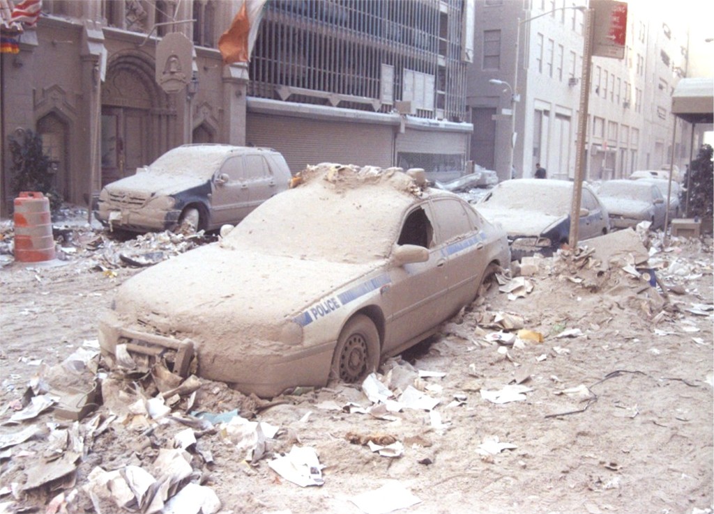 Police cars and a street in Lower Manhattan buried in dust and debris after the towers collapsed