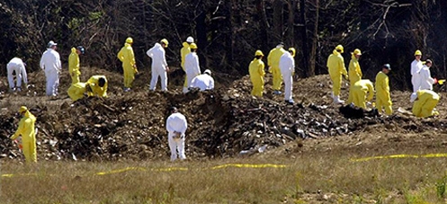 Investigators and recovery workers in yellow and white protective suits at the Flight 93 crash site in Shanksville, Pennsylvania