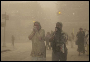 People covering their faces as they walk through thick dust and debris after the towers collapsed